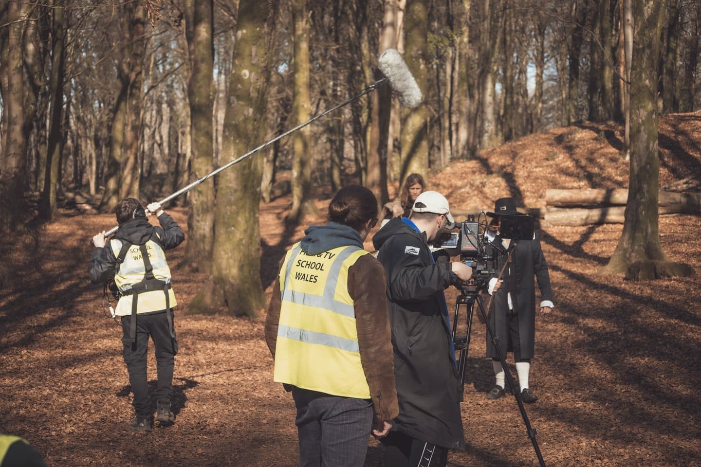 Una troupe cinematografica gira una scena in una foresta soleggiata e piena di foglie.