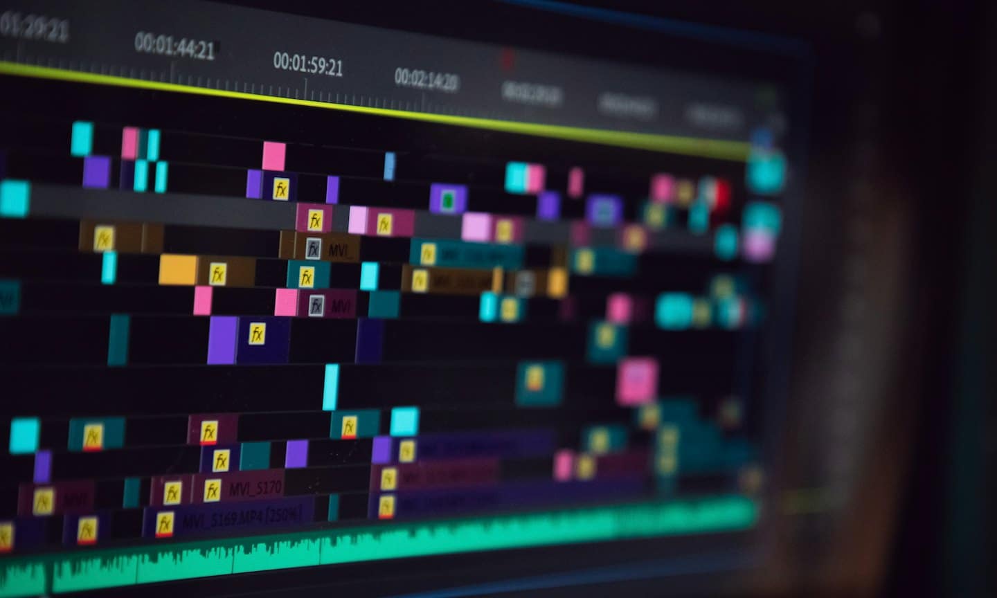 Timeline di montaggio video con clip colorate e codici temporali su uno schermo.